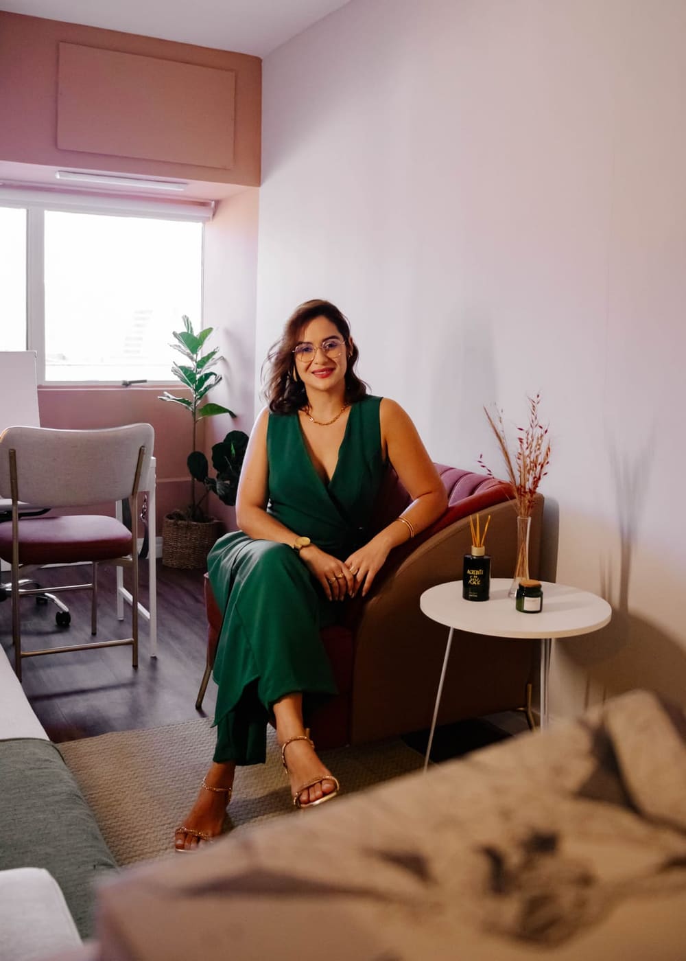 Maylanne Moreira, psicóloga, sentada em seu consultório, sorrindo para a câmera em um ambiente com luz natural e plantas